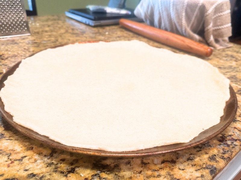 rolled out pizza dough on a pizza pan in process image 