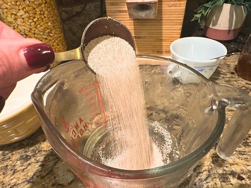1 Tbsp yeast being poured into measuring cup of warm water